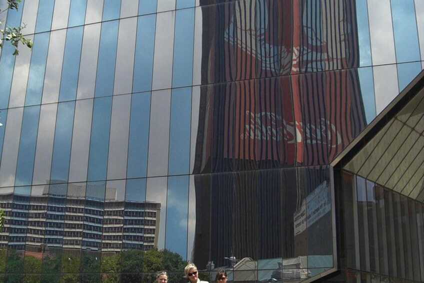 A modern building with reflective glass windows and a visible reflection of a red structure. 1