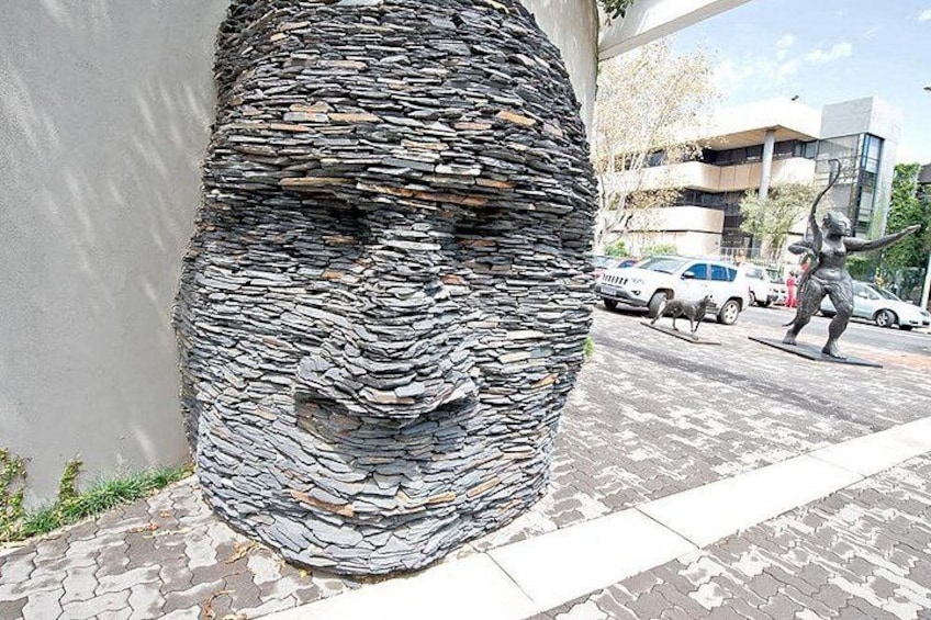 A textured sculpture resembling a face on a building facade, with cars and a pedestrian in the background. 4