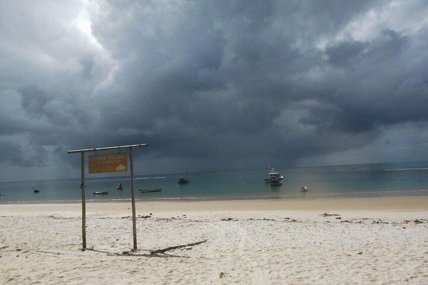 Een strand met een bord, rustige zee en boten in de verte, onder een bewolkte lucht. 5
