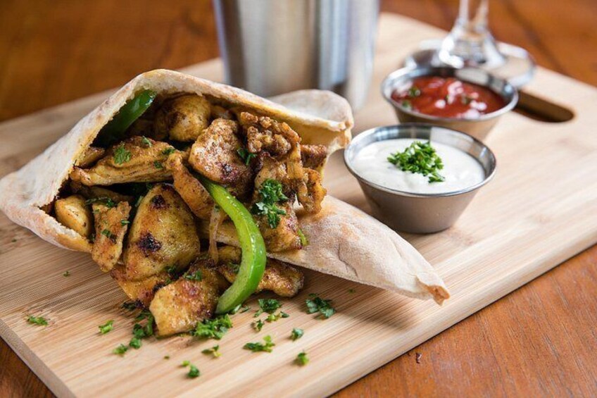 A wrap with grilled chicken and vegetables, a bowl of sauce, and a metal cup on a wooden board. 5