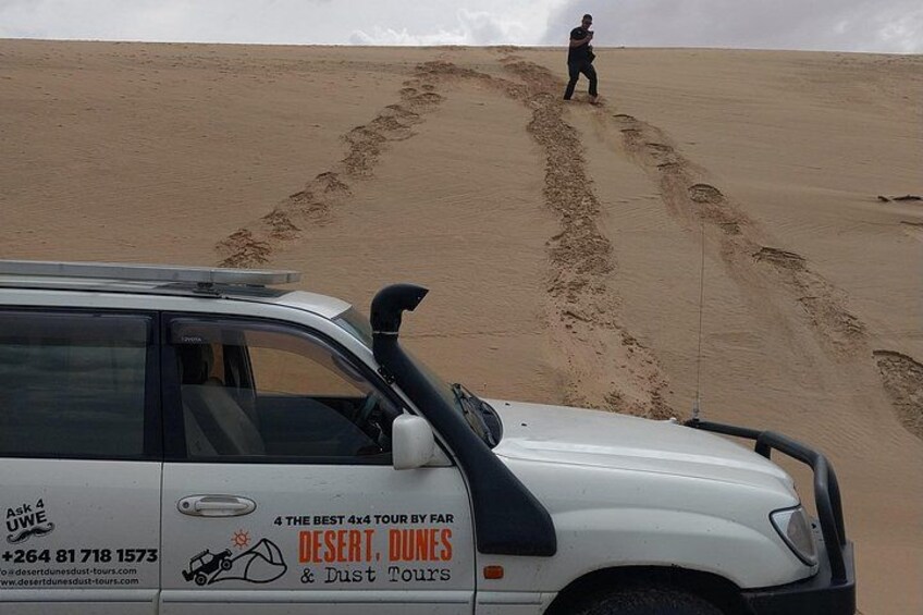 En hvid SUV med en annonce for ørkenture, parkeret på en sanddune med fodspor, der fører væk. 5