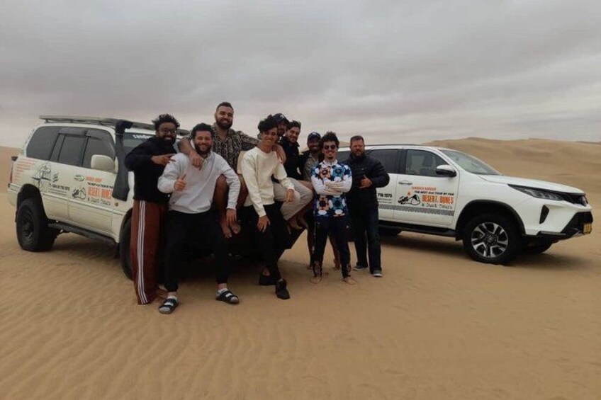 Un groupe de personnes posant à côté d’un VUS blanc dans un paysage désertique. 2