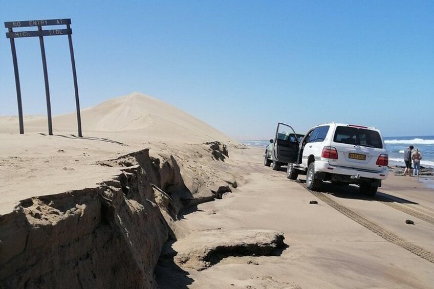 A white SUV parked on a sandy beach with a large sand dune in the background. 5