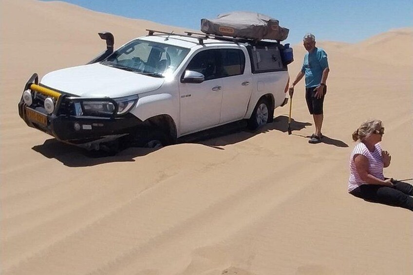 A white SUV with a roof rack and luggage on a sandy dune. 4