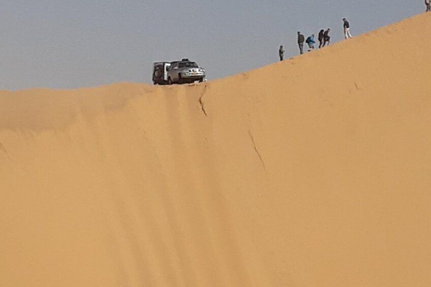 A vehicle on a sand dune with people standing on the top. 2