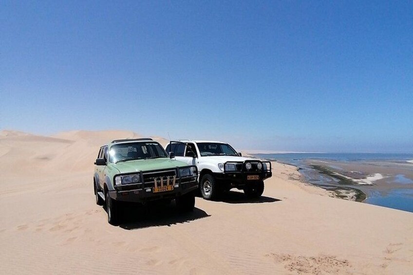 Two off-road vehicles parked on a sand dune with a beach in the background. 3