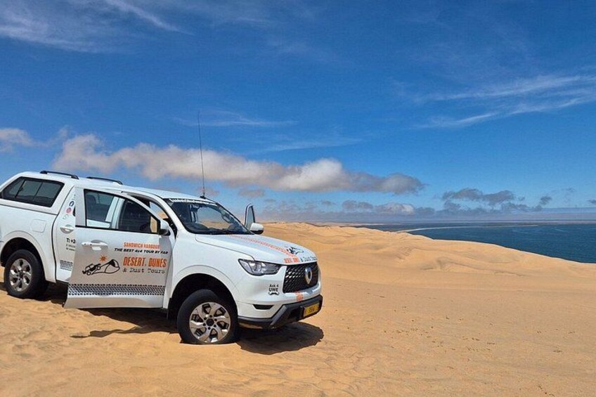 A white SUV parked on a sandy dune with a clear blue sky and a body of water in the background. 5