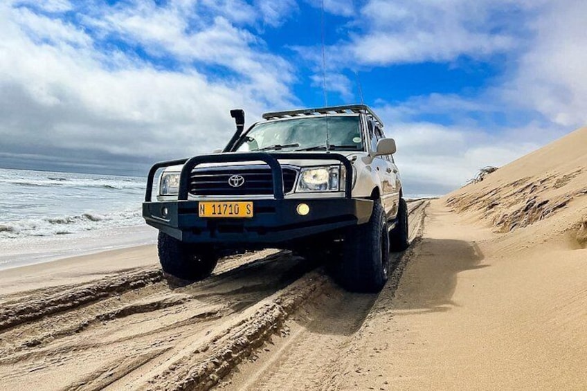 A white off-road vehicle on a sandy beach with the ocean in the background. 4