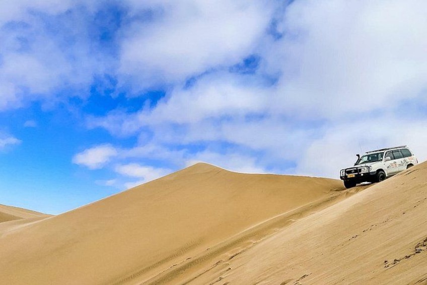 A white vehicle navigating a sandy dune landscape under a partly cloudy sky. 4