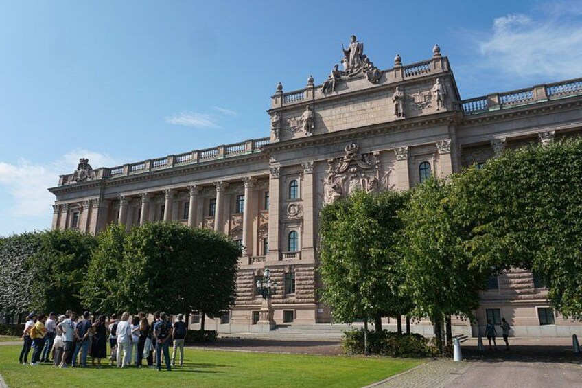 Ein gro ßes, verziertes Gebäude mit Säulen und Statuen, umgeben von gepflegten Rasenflächen und Bäumen. 3