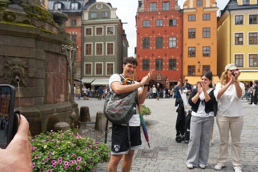 Ein Kopfsteinpflasterplatz mit historischen Gebäuden, einem Brunnen und Menschen, die Fotos machen. 4