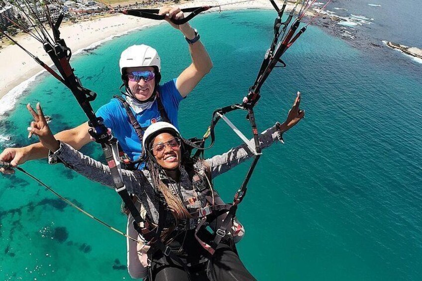 En person paraglider over turkis vand med en strand i baggrunden. 2