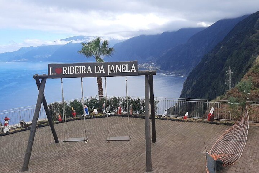 Altalena con un cartello che recita “I love Ribeira da Janela” affacciata su un paesaggio costiero con montagne e mare. 4