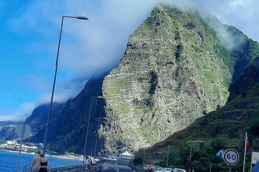 Una strada costiera con una montagna, un segnale di limite di velocità e un lampione. 2