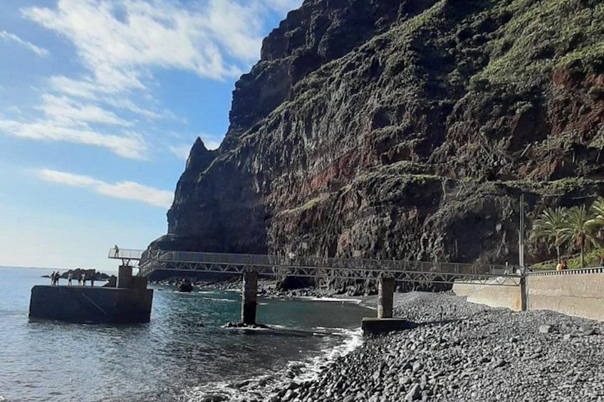 A rocky beach with a bridge over water, cliffs in the background, and a clear sky. 3