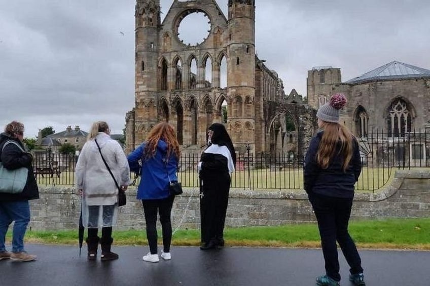 A group of people standing in front of a historic stone building with a large circular window and arched doorways. 2
