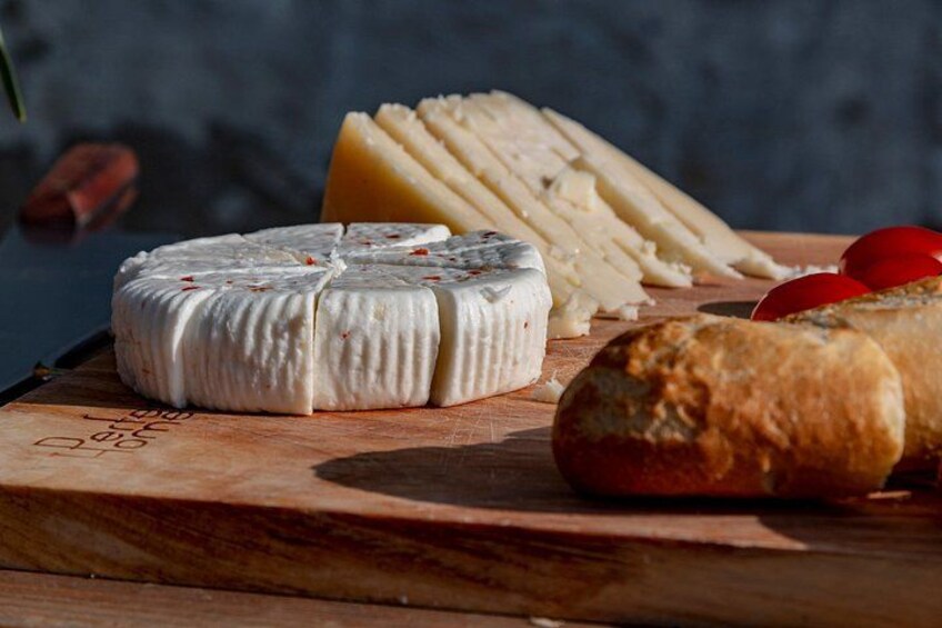 Una ruota di formaggio, fette di formaggio, pomodori e pane su un tagliere di legno. 3