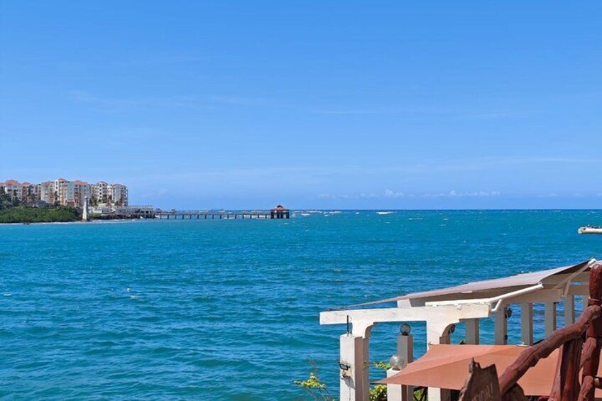 Un paysage côtier avec une jetée qui s’avance dans la mer, des bâtiments sur une portion de terre à proximité et un ciel dégagé. 5