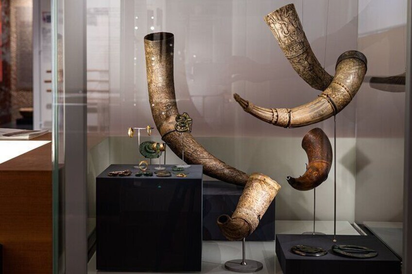 A museum display with ancient artifacts, including a large curved horn and a smaller, coiled horn. 5