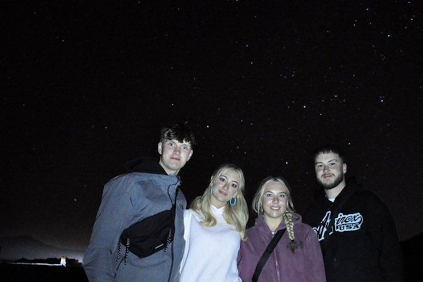 Four people standing outdoors at night with a starry sky in the background. 4