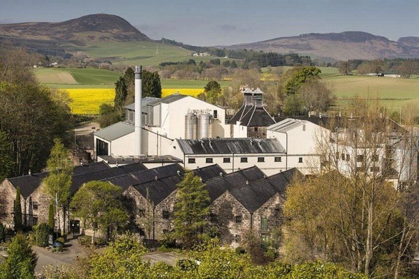 A large industrial building with a chimney, surrounded by trees and fields. 2