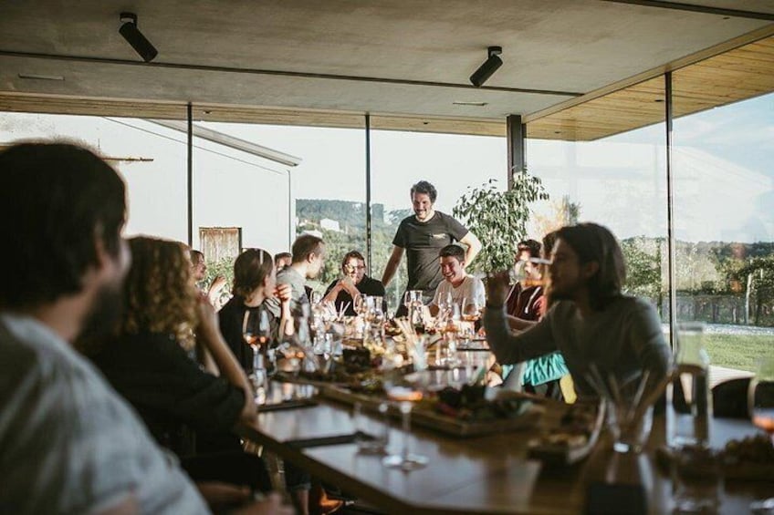 Un grupo de personas sentadas alrededor de una mesa en un comedor moderno y abierto, con amplios ventanales. 1
