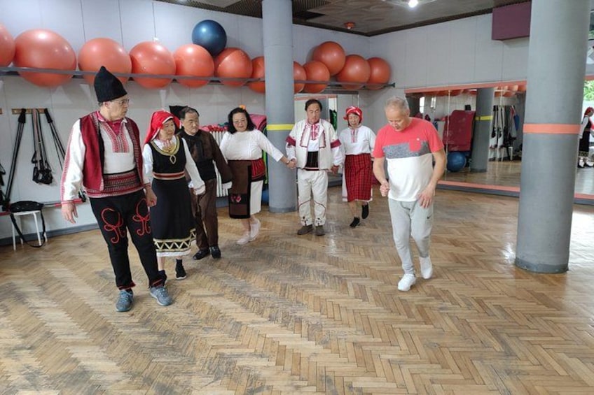 Mensen in traditionele kledij lopen door een sportzaal met fitnessballen en houten vloer. 1