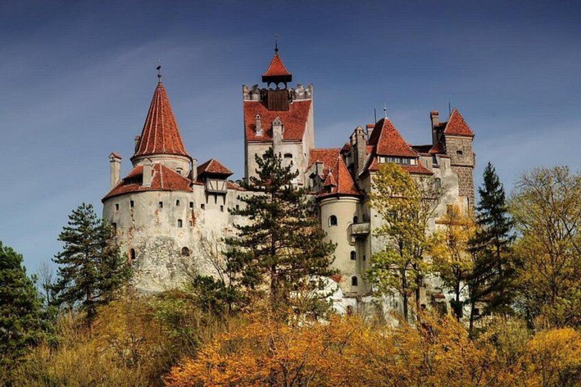 Un château doté de nombreuses tours et de toits rouges, entouré d’arbres et de feuillages d’automne. 2
