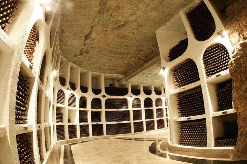 A wine cellar with rows of wine bottles, arched ceilings, and a circular central area. 2