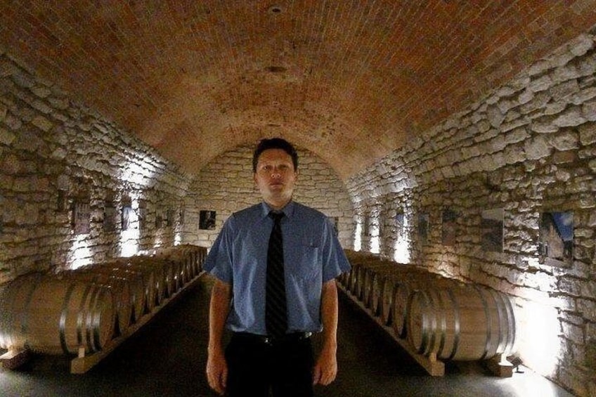 A man standing in a wine cellar with stone walls and large wine barrels. 1