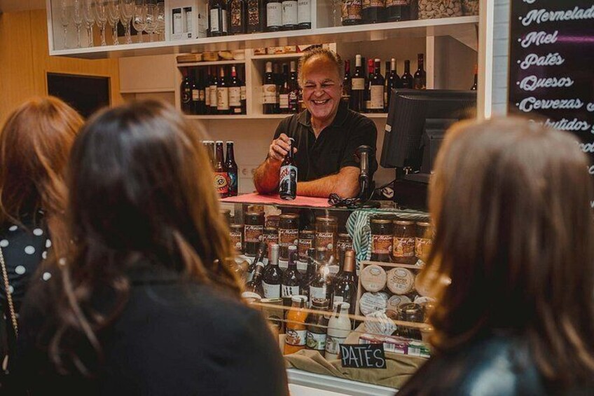 A person behind a counter with various bottles and jars, a menu board with items listed, and a display case with more bottles. 2