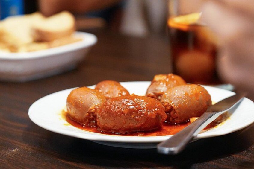 A plate of stuffed cabbage rolls with a red sauce, a fork, and a blurred background of a dining table. 5