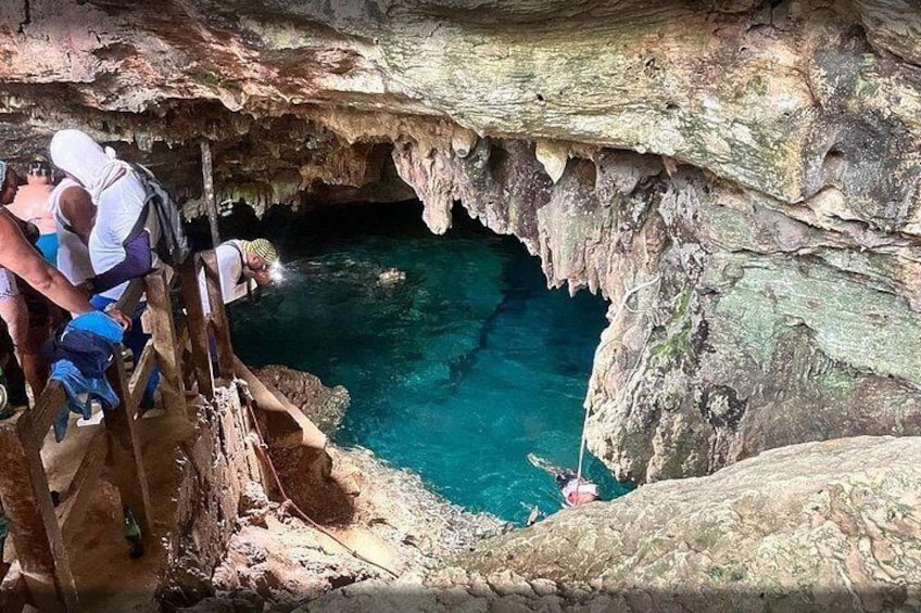 Una cueva con una piscina azul cristalina, escaleras de madera y gente explorando. 1
