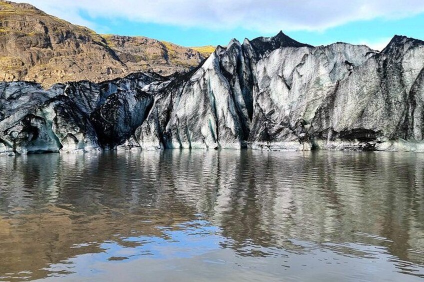 A glacier with a reflective water surface, rugged terrain, and a clear sky. 3