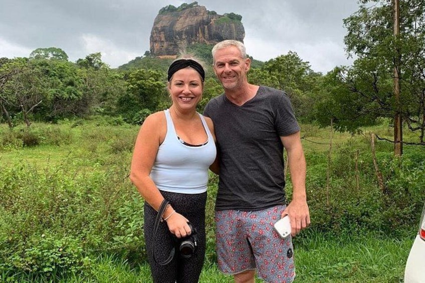 Two people standing in a grassy area with a large rock formation in the background. 1