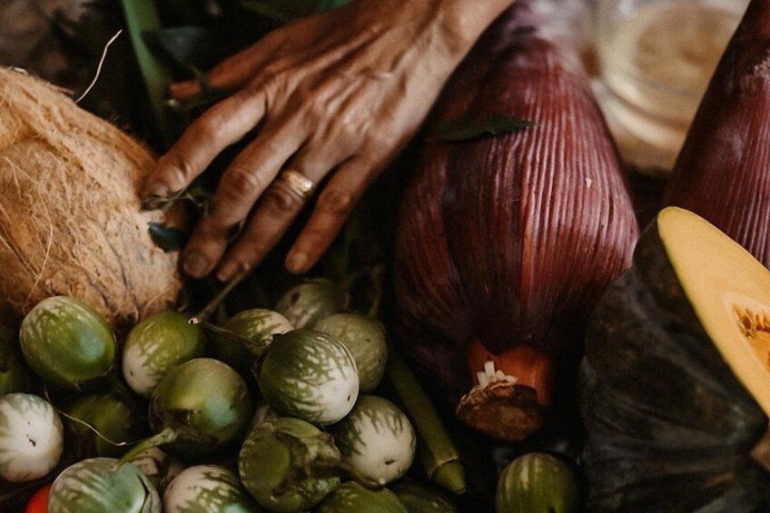 A variety of vegetables including onions, a coconut, and green fruits. 2