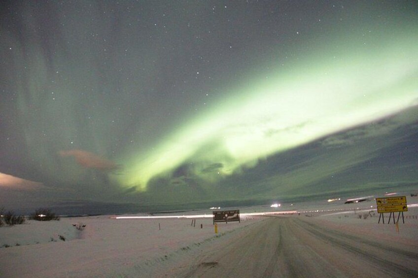 Ett snöigt landskap med en väg, en skylt och norrsken. 3