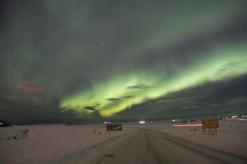 A snowy road with a sign, under a night sky with the aurora borealis. 4