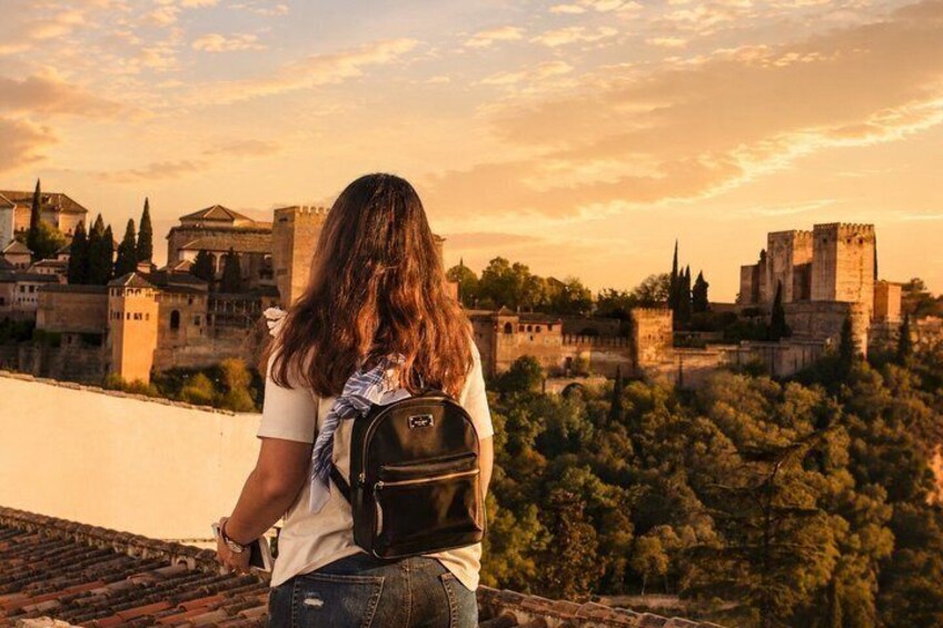 A person with a backpack overlooking a historic cityscape with ancient buildings and a castle. 3