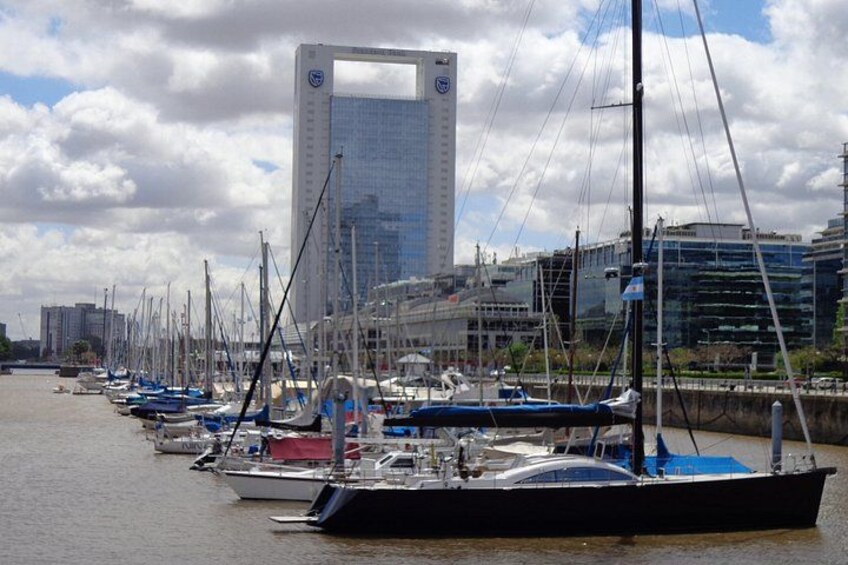 A marina with boats docked, a large building with a distinctive window, and a cityscape in the background. 2