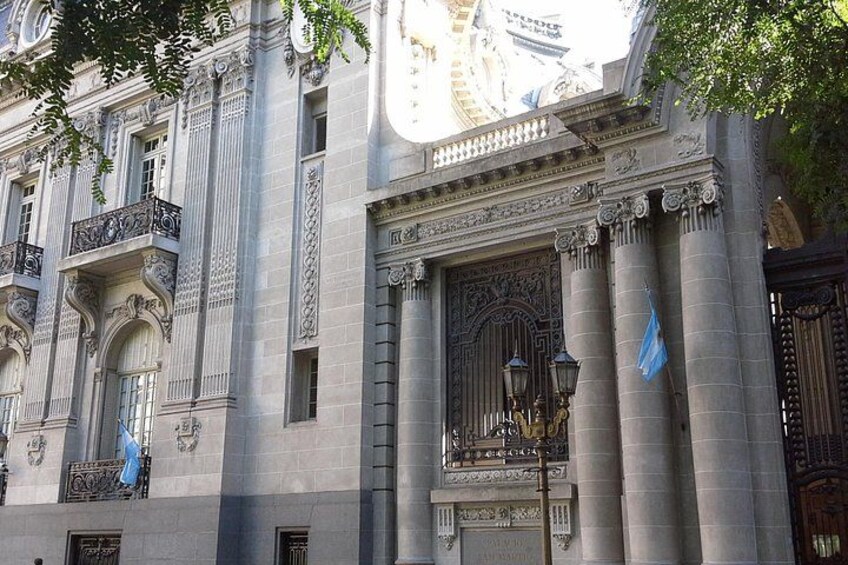 A classical building with ornate columns, a large arched window, and a flag. 4