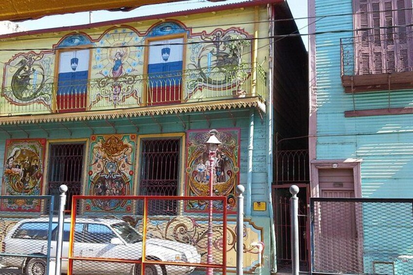 A colorful building with intricate murals, a metal fence, and a parked car. 2