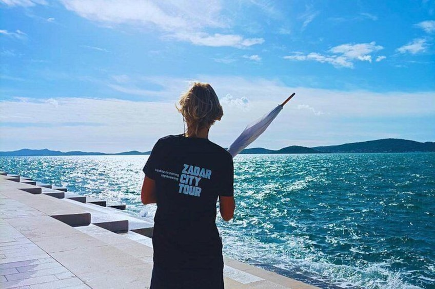Una persona in piedi vicino al mare indossa una maglietta con la scritta 'ZADAR CITY TOUR'. 2