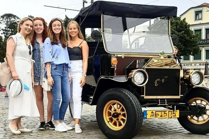 Fyra personer står framför en klassisk bil med guldfärgade fälgar och en svart kaross. 1