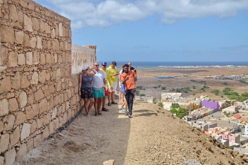 Un grupo de personas de pie sobre un muro de piedra con vista a un pueblo costero. 1