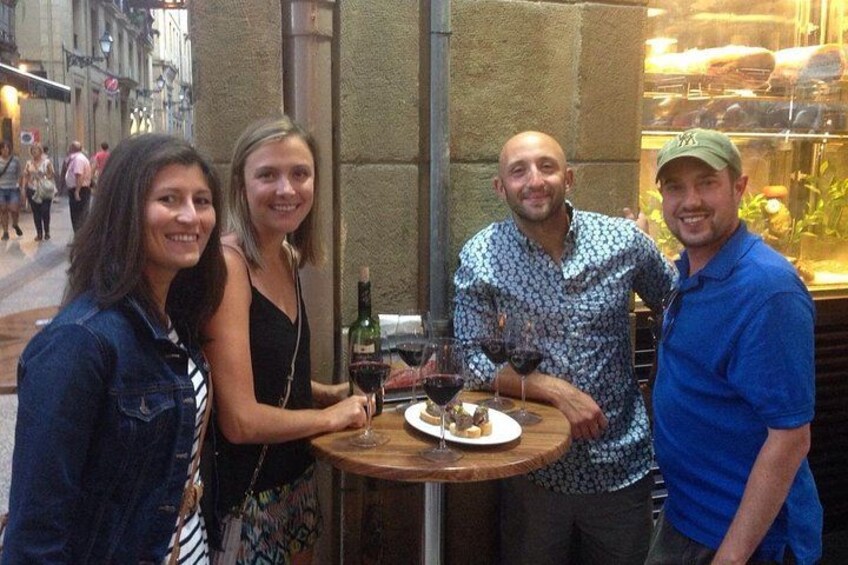 A group of people sitting at a round table with wine glasses and a bottle of wine. 1