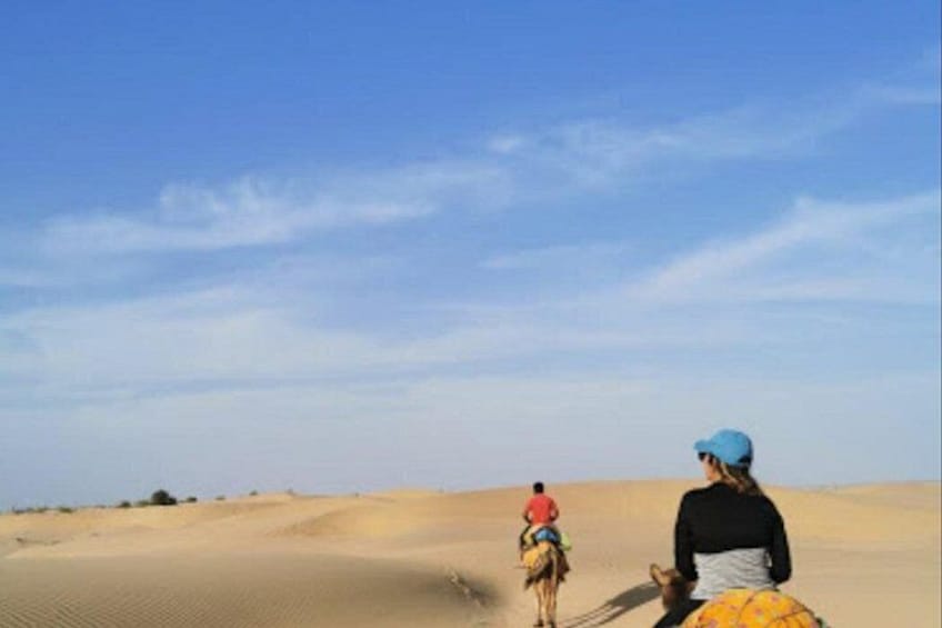 Dos personas montando camellos en un desierto con dunas de arena. 3