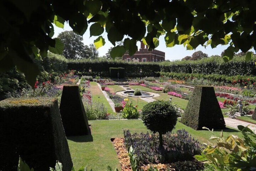 A formal garden with geometric hedges, a central fountain, and a distant building. 2