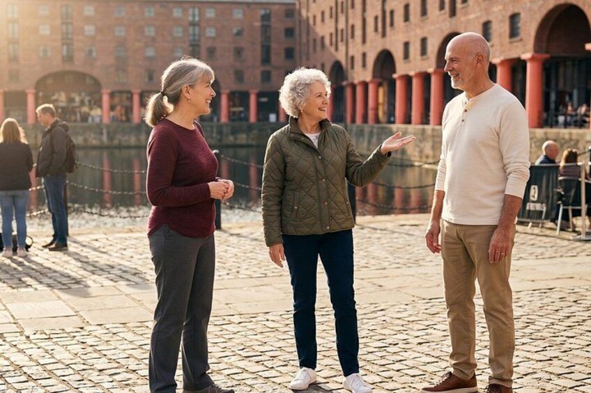 Drie mensen staan op een geplaveid pad, met een historisch gebouw op de achtergrond. 1