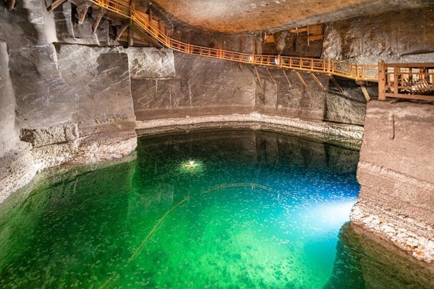 Een groot, natuurlijk zwembad met helder turquoise water, omgeven door rotswanden en houten looppaden. 3